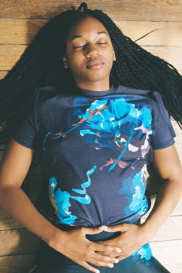 Woman lying in savasana wearing a Take It Easy Honey t-shirt with black flower print made from recycled fabrics. super comfortable fit